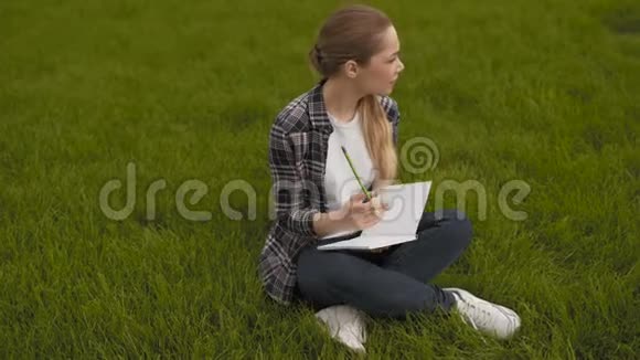 少女坐在草地上在笔记本上做笔记十几岁的女孩坐在草地上在笔记本上记笔记4K视频的预览图