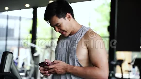 亚洲运动员在健身房用手机健身中心有智能手机的年轻人视频的预览图