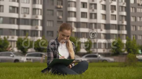 学生女孩坐在公园的草地上在4K的笔记本上做笔记视频的预览图