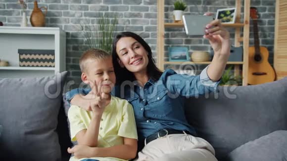 漂亮的女孩妈妈和可爱的儿子一起自拍微笑着举着智能手机视频的预览图