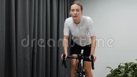 女人骑着固定的自行车在室内骑自行车专注女性在室内智能自行车训练器上进行健身训练视频的预览图