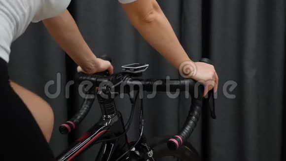 女人在室内骑自行车用自行车电脑和车轮在车把上近距离观看智能自行车培训师的室内培训视频的预览图