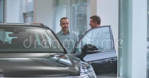 两个成熟的白人男子站在黑色汽车旁边握手男性汽车经销商与视频的预览图
