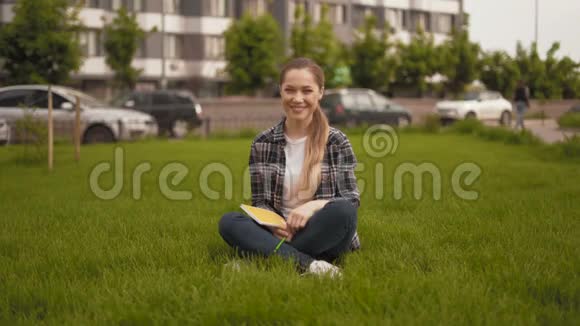 竖起大拇指远射20岁的女孩穿着格子衬衫坐在草地上真诚地笑了视频的预览图