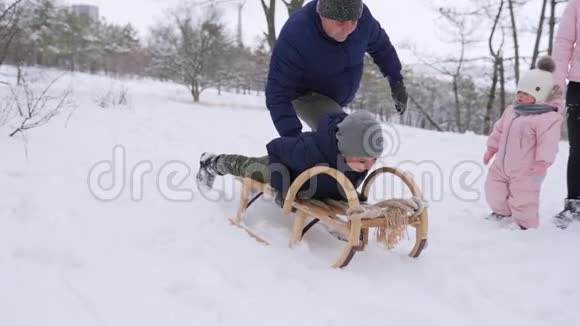父亲在公园里下雪的冬天把儿子推下山户外雪橇男孩幸福的家庭在哭泣视频的预览图