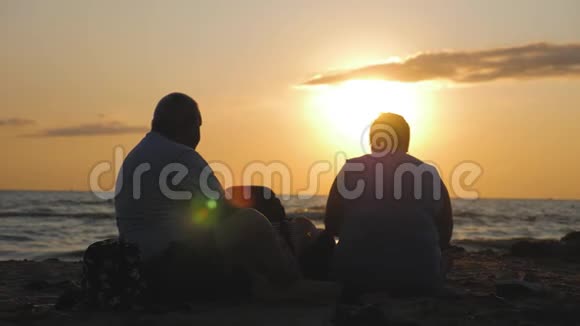日落时分一对老年夫妇坐在海滩上欣赏美丽的海景和海景视频的预览图