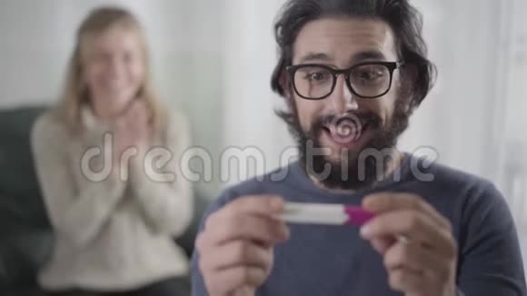 面对震惊的白人男子举行怀孕测试回头看他的妻子或女朋友拍手和微笑视频的预览图
