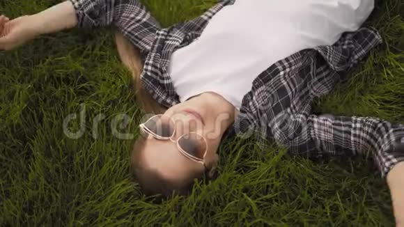 特写肖像年轻快乐的女孩正躺在草地上微笑带4K眼镜的女人脸视频的预览图