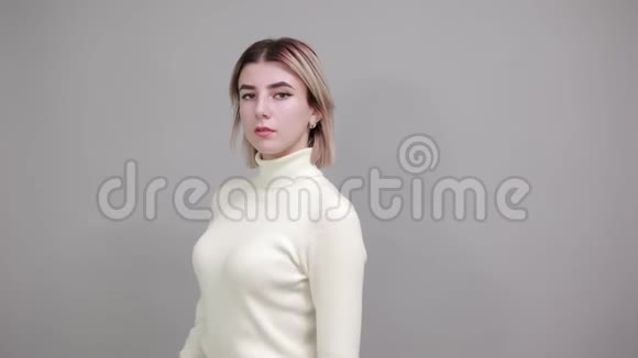 穿着白色毛衣的严严实实的年轻女子双手托着下巴越过灰色的墙壁视频的预览图