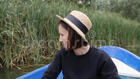 年轻的白种人女孩戴着草帽在船上划船微笑着快乐的女孩在湖边公园玩得很开心性感的黑发女孩视频的预览图