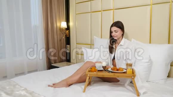 漂亮的年轻女人早上在床上吃早餐成功的女性旅行者享受早晨咖啡视频的预览图