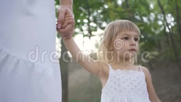 一个金发小女孩牵着妈妈的手在公园里走来走去家庭幸福一个家长母亲视频的预览图