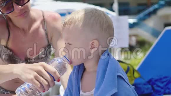 在阳光明媚的夏日妈妈在海滩上给一个小儿子喝水视频的预览图
