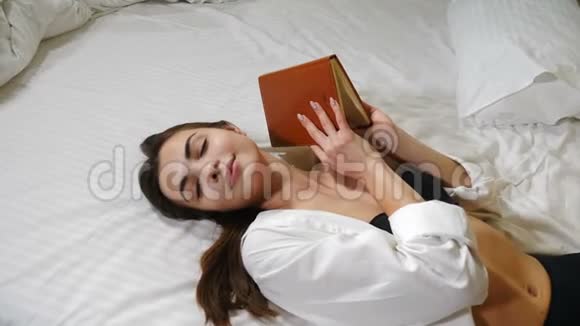 美丽的年轻女士躺在大床上手里拿着一张写字纸在家里放松旅馆里漂亮的女人视频的预览图