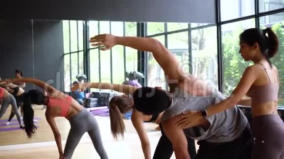 亚洲年轻瑜伽女教练协助男性初学者平衡灵活姿势在课堂上的健身房工作室瑜伽和瑜伽视频的预览图