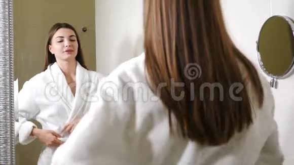 快乐的年轻女人早上在浴室镜子前跳舞穿着白色长袍的滑稽迷人的女人欢快地跳舞视频的预览图