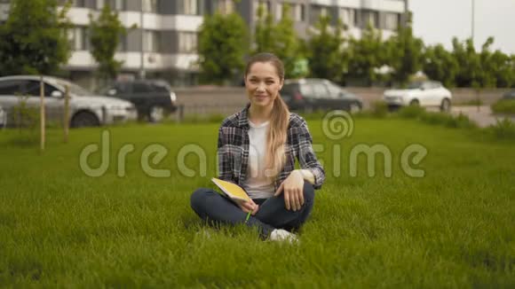 手势好的远射20岁的女孩穿着格子衬衫坐在草地上真诚地笑了视频的预览图