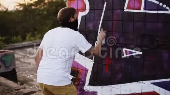 一个穿着黑色巴拉克拉瓦和白色T恤的人的背面景色使他在街墙上的艺术作品完成了修正视频的预览图
