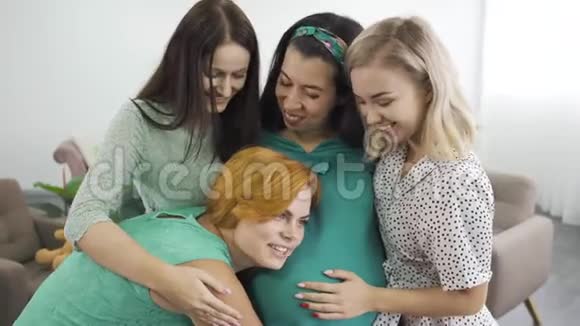 四个年轻迷人的白种人女人拥抱和微笑红头发的女孩听着朋友肚子里孩子说话视频的预览图