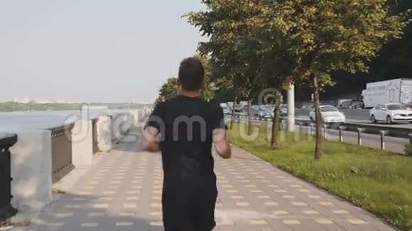 清晨穿着黑色T恤和运动短裤的年轻运动员沿着长廊奔跑一个身材魁梧的男人视频的预览图
