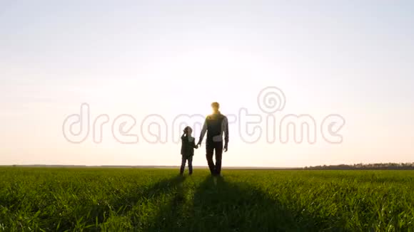 快乐的父亲和儿子在美丽的夕阳下走上一片绿色的田野幸福家庭的剪影视频的预览图