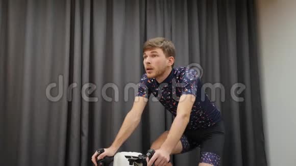 男性运动员骑着智能自行车教练从马鞍上骑自行车在家骑自行车的小男孩骑着自行车无主虚拟自行车视频的预览图