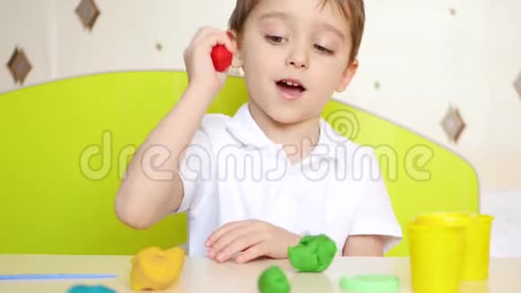 一个小男孩坐在桌子旁玩着明亮的粘土视频的预览图
