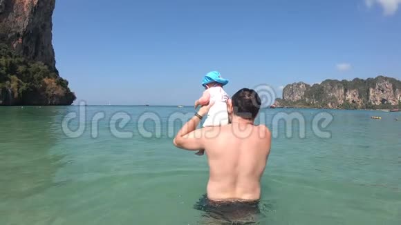 父亲在晴朗的晴天在海里给婴儿洗澡视频的预览图
