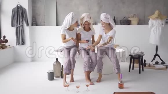 三个漂亮的女朋友穿着同样的睡衣头上有毛巾在一起看手机视频的预览图