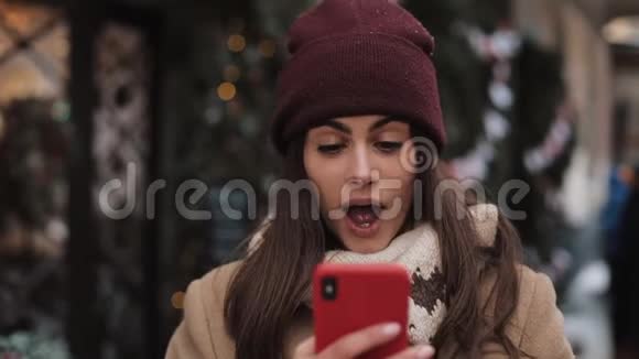 冬天帽子里漂亮女孩的特写镜头用智能手机聊天看着屏幕看着视频的预览图