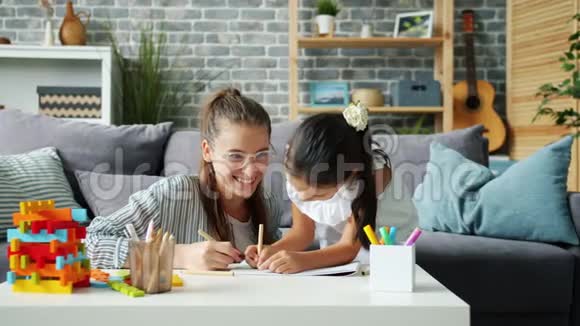 快乐的小女孩在家里和有爱心的妈妈一起用铅笔玩视频的预览图