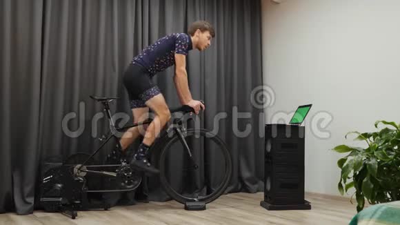 在自行车家庭教练上进行艰苦的训练在业余时间骑自行车时男性在智能自行车教练身上做有氧运动视频的预览图