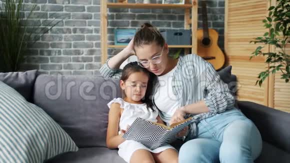 母亲和女儿在家看书微笑着在沙发上放松视频的预览图