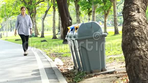 亚洲女人从地板上捡垃圾到垃圾桶女人在公园的草地上捡垃圾塑料袋视频的预览图