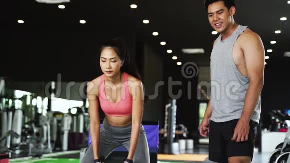 亚洲私人教练指导一名健美女子在健身馆进行交叉式绳索练习视频的预览图