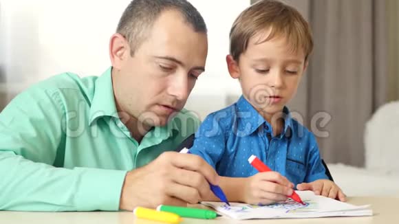 父亲和一个小男孩画着画坐在桌子旁画着彩色的记号一个慈爱的父亲花时间和他的孩子在一起这就是视频的预览图