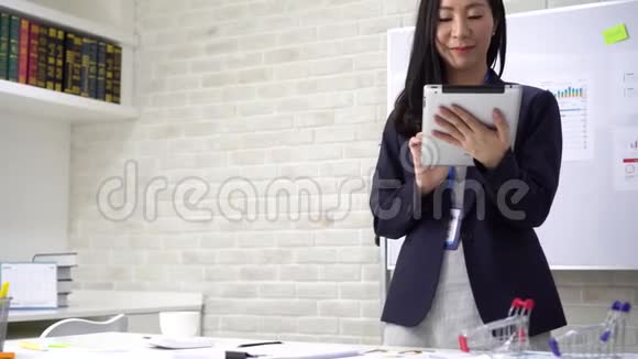 亚洲女商人在办公室喝咖啡时使用平板电脑视频的预览图