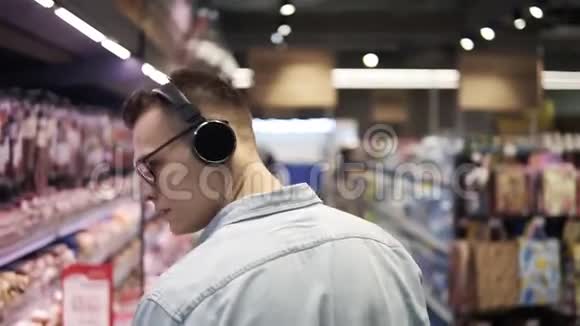 在超市时尚的白种人带着耳机走过商店的肉制品部分在后面视频的预览图