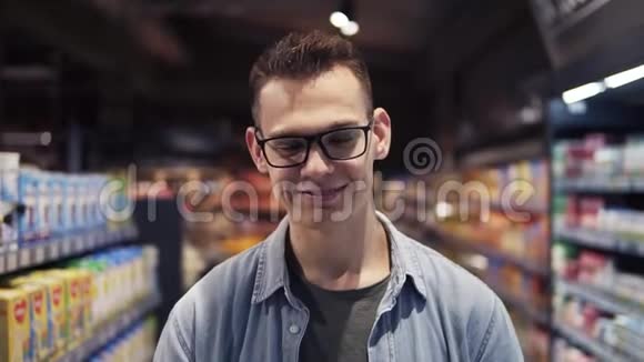 在超市里一个年轻英俊的白种人戴着眼镜在超市里购物兴高采烈地微笑着视频的预览图