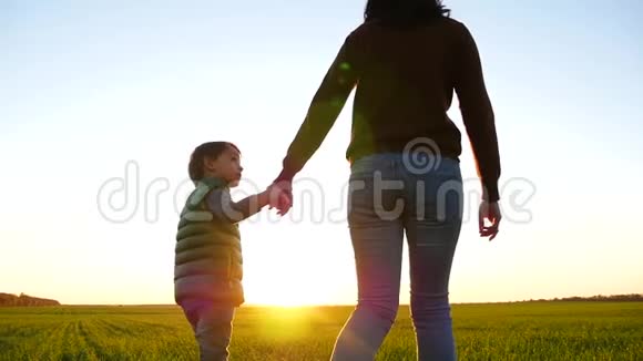 一个孩子和他的母亲一起散步在美丽的夕阳背景下牵着她的手可爱的男孩看着他视频的预览图