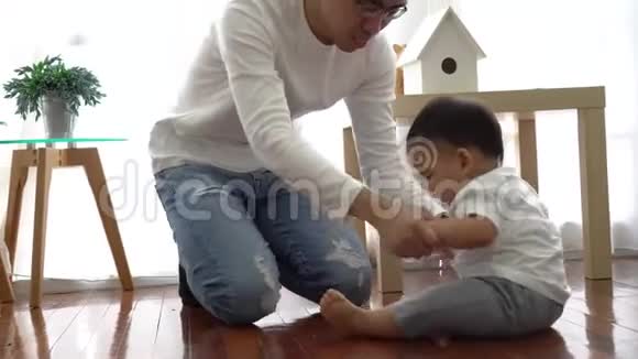 严肃的亚洲小男孩在地板上爬行而年轻的父亲坐在他旁边的客厅里视频的预览图