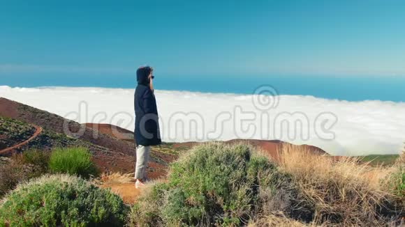 迷人的女人站在悬崖边从高山上看到的云和森林全景视频的预览图