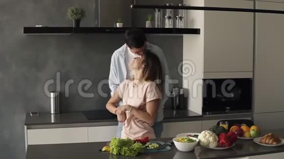 漂亮的年轻白种人夫妇一大早就在家现代厨房见面站在柜台前拥抱视频的预览图