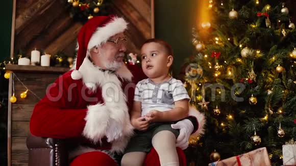 小男孩窃窃私语圣诞老人听他说圣诞愿望坐在他的大腿上视频的预览图