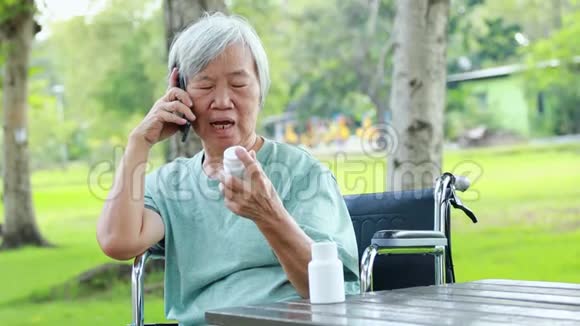 患病的亚洲老年妇女拿着一瓶药打电话询问医生担心老年女性咨询询问视频的预览图