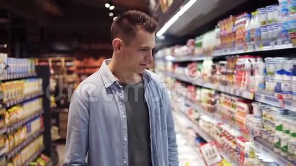 超市里一个漂亮的高个子穿着蓝色衬衫从冰箱里挑选新鲜牛奶的白人微笑的年轻人视频的预览图
