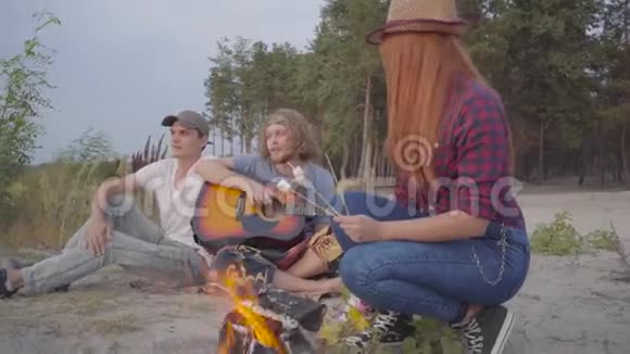 年轻的时髦朋友在海滩上玩着玩火做棉花糖在背景上弹吉他视频的预览图