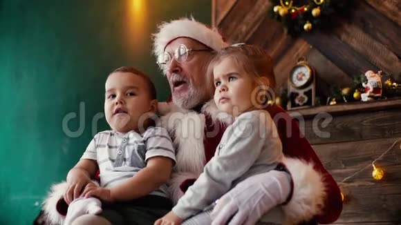 小男孩和小女孩坐在圣诞老人的腿上房间里有节日的内部视频的预览图