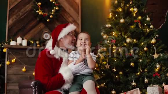 小可爱的男孩许愿坐在圣诞老人的圈里在圣诞树旁边视频的预览图