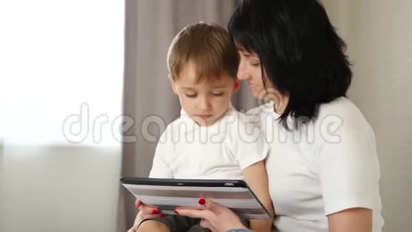 母亲和她的小儿子用平板电脑看电影玩游戏或者打电话视频的预览图
